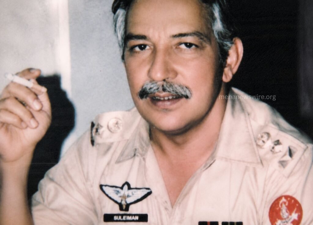 - MENA News Wire Man in a tan military uniform smoking a cigarette, facing the camera with patches and insignia visible on the shirt.